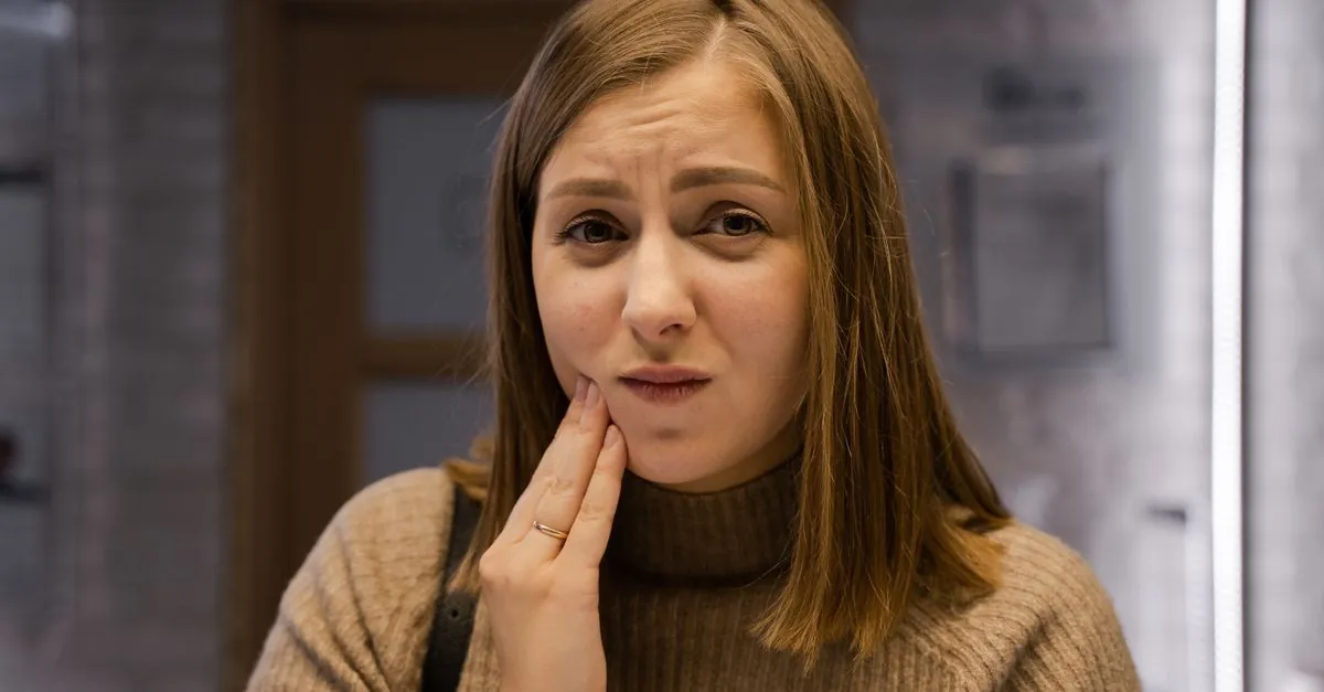 Femeie care își ține obrazul din cauza unei dureri dentare